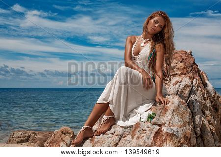 sensual young woman sitting on the rock on the beach