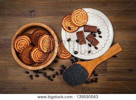 There are Cookies,Candy,Chocolate Peas,Poppy;Porcelain Saucer,Tasty Sweet Food on the Wooden Background,Top View