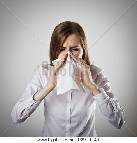 Young slim woman in white is sneezing.