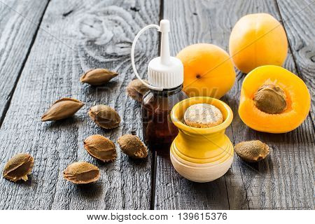 Essential oil from apricot kernels in small brown bottles and small yellow clay jar fresh apricots and apricot seeds on a dark wooden table