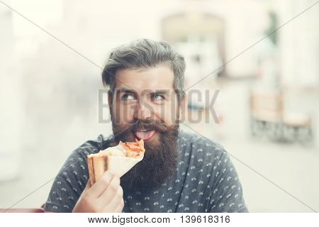 handsome sexy bearded young man hipster with long beard and mustache on smiling hairy face eating pizza on street outdoor