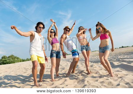 Rise your mood. Cheerful jubilant smiling friends standing on the sand and feeling glad while having fun on the beach