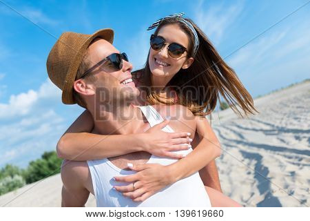 Happy with you. Cheerful handsome smiling man holding his girlfriend on the back and expressing joy while resting together on the beach