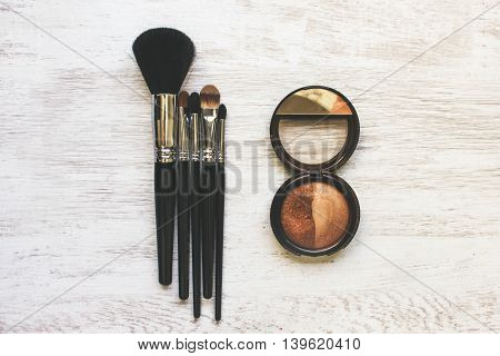 Brushes for cosmetics and powder are laid out on a white wooden table