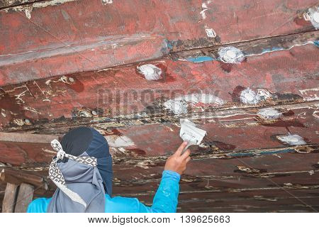 Woman Worker Filling Wood Filler Under Fishing Boat