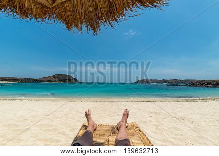 Legs of guy relaxing on sandy beach under umbrella