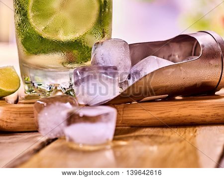 Chunks of ice cubes alcohol drink background on wooden boards. Part of drink number two hundred fifty four cocktail mohito with slice lime and mint leaf.