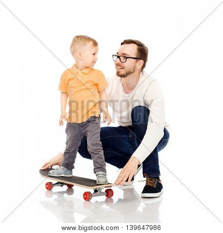 family, childhood, fatherhood, leisure and people concept - happy father teaching little son to ride on skateboard