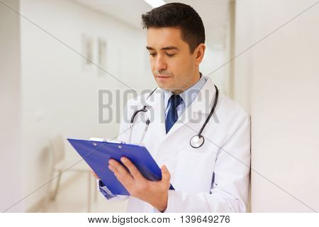 medicine, healthcare and people concept - doctor writing to clipboard at hospital