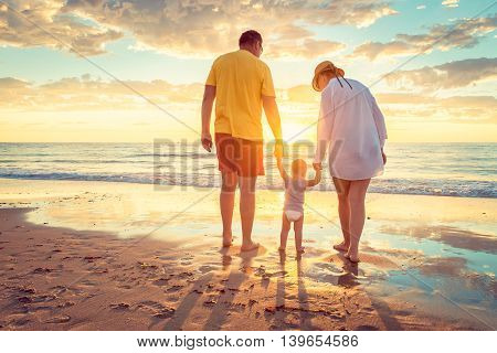 Grandfather and grandmother with grandson holding hands of each other on the beach at susnet. Color-toning applied.