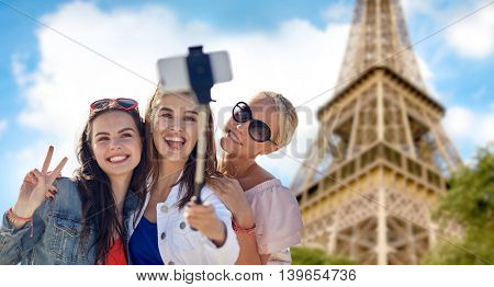 summer vacation, holidays, travel, technology and people concept- group of smiling young women taking picture with smartphone on selfie stick over eiffel tower in paris background