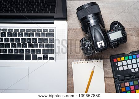 Top view of photographer working desk with laptop, camera and notebook