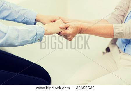 people, age, family, care and support concept - close up of senior and young woman  holding hands