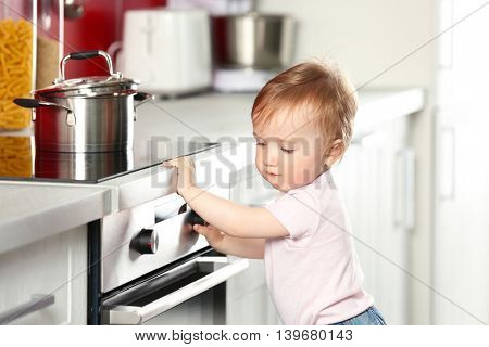 Little child playing with pan and electric stove in the kitchen