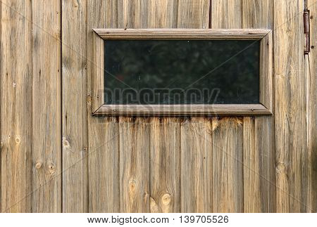 A small closed window in unpainted rustic wooden wall of a wooden house horizontal view
