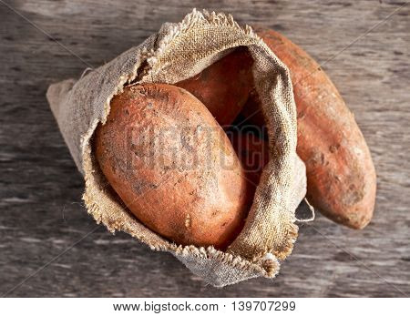 Freshly harvested organic sweet potatoes in a burlap bag on wooden table