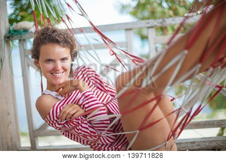 Portrait young sexy girl relaxing on beach Bungalow in hammock. Smiling woman spending chill time outdoor summer. Caribbean Ocean Vacations. Horizontal, blurred background