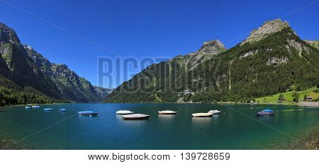 Summer day at lake Klontalersee Switzerland. Boats on turquoise water. High mountains and green forest.