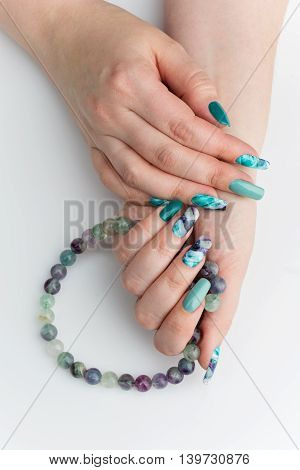 Closeup of woman nails with creative purple and green manicure. Fluorinit print. Natural stone beads. Copy space.