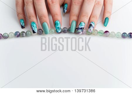 Closeup of woman nails with creative purple and green manicure. Fluorinit print. Natural stone beads. Copy space.