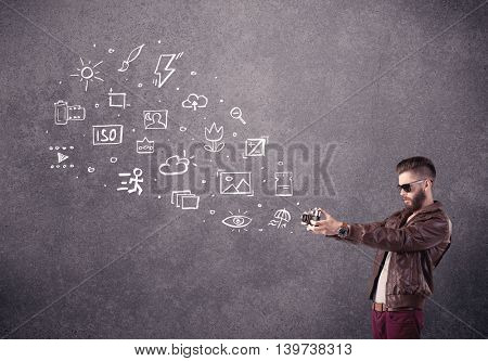 An elegant hipster guy trying to use a vintage camera with camera settings icons drawn on wall, like flash, white balace or ISO value concept