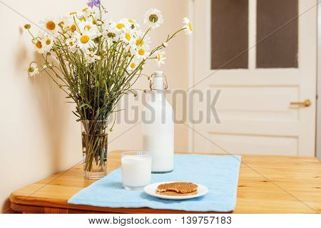 Simply stylish wooden kitchen with bottle of milk and glass on table, summer flowers camomile, healthy foog moring concept noone