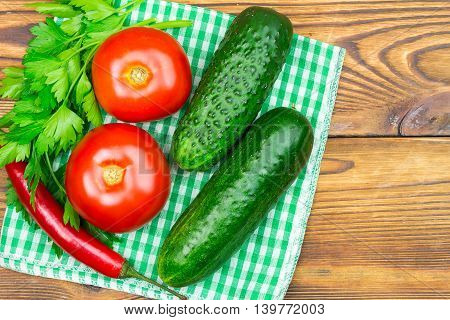 Backyard vegetables tomatoes cucumber chilli pepper and parsley on napkin wooden background top view