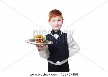Little waiter stands with tray serving hamburger. Smiling redhead child boy in suit plays restaurant servant, gives burger isolated at white background