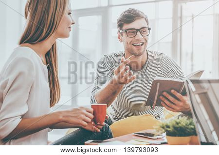 Sharing great ideas. Cheerful young man holding note pad and gesturing while sitting in office with his colleagues