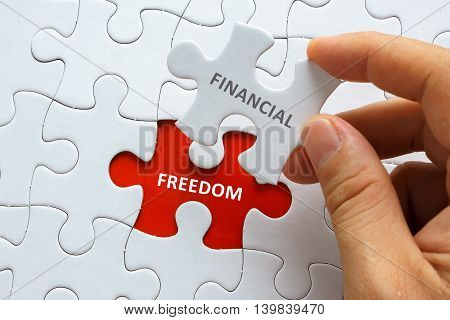 Hand Holding Piece Of Jigsaw Puzzle With Word Financial Freedom.