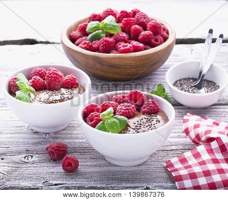 Chocolate banana smoothies with chia seeds served ripe raspberries and fresh mint on a light wooden background. The white ceramic bowls of serving a healthy breakfast. selective focus