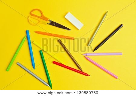 Color pencils and scissors on yelloow paper background