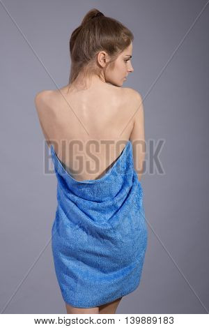 Rear view of beautiful woman with brown hair wearing blue towel against gray background