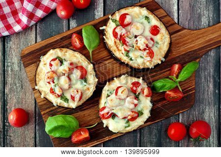 Healthy Eggplant Mini Pizzas With Melted Mozzarella, Tomatoes And Basil On A Serving Board Against R