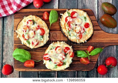 Healthy Eggplant Mini Pizzas With Melted Mozzarella, Tomatoes And Basil On A Serving Board Against R