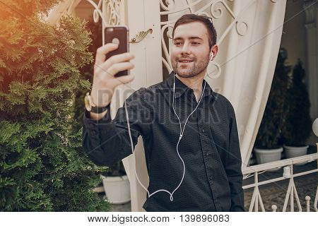 A guy in a nice town, walking, listening to music and taking pictures themselves on the phone