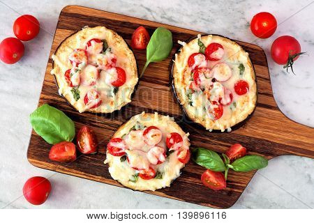 Healthy Eggplant Mini Pizzas With Melted Mozzarella, Tomatoes And Basil On A Serving Board Against M
