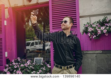 A guy in a nice town, walking, listening to music and taking pictures themselves on the phone