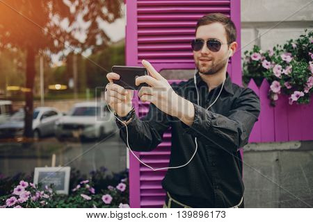 A guy in a nice town, walking, listening to music and taking pictures themselves on the phone