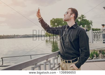 A guy in a nice town, walking, listening to music and taking pictures themselves on the phone