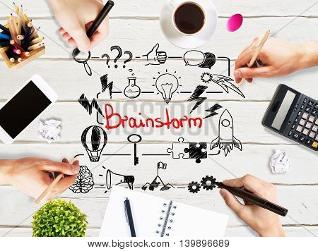 Brainstorm concept with businesspeople hands drawing sketch on light wooden office desktop with blank smartphone coffee cup stationery and other items