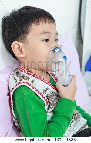 Asian Child Holds A Mask Vapor Inhaler For Treatment Of Asthma. Breathing Through A Steam Nebulizer.