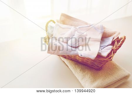 clothing, babyhood, motherhood and object concept - close up of white baby bootees with pile of clothes and towel for newborn boy in basket on table