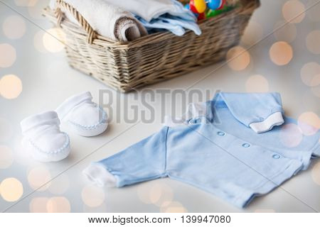 clothing, babyhood, motherhood and object concept - close up of white baby bootees with pile of clothes and towel for newborn boy in basket on table