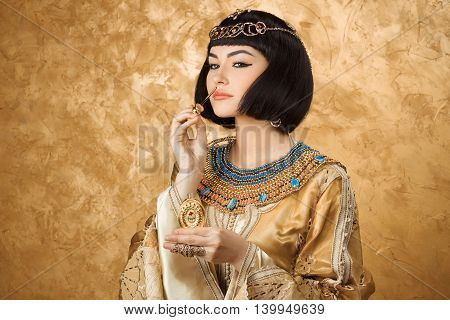 Young girl with perfume bottle. Glamorous closeup portrait of beautiful sexy stylish brunette young woman model with bright makeup with gold jewelery. Cleopatra