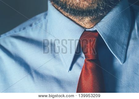 Businessman in blue shirt and red necktie in office with strong shadows suitable for intense business situation such as meeting or contract assignment with uncertain outcome selective focus.