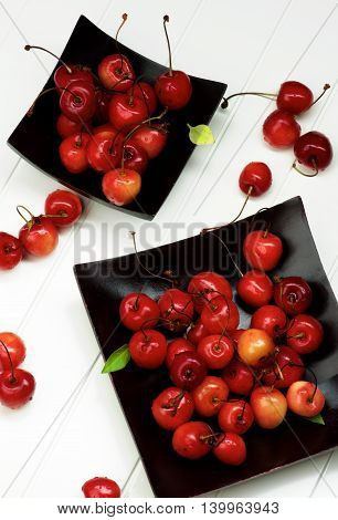 Arrangement of Fresh Ripe Sweet Maraschino Cherries in Black Wooden Plates closeup on Plank White background. Top View
