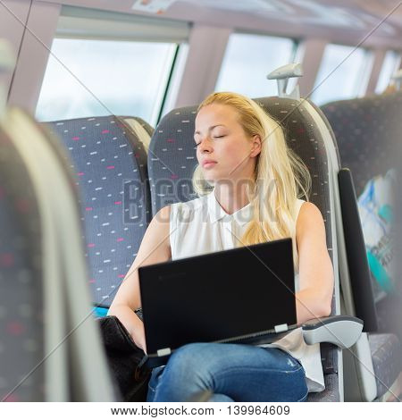 Businesswoman naping sitted while traveling by train and working on laptop. Tiresome business travel.