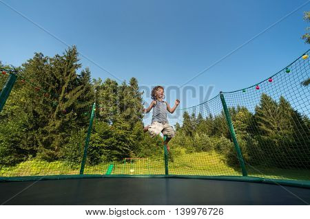 Cute boy enjoys jumping and bouncing on trampoline oudoors.