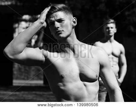 Young man sexy muscular bodybuilder macho with bare torso stylish haircut while twin brother poses outdoor black and white on blurred background